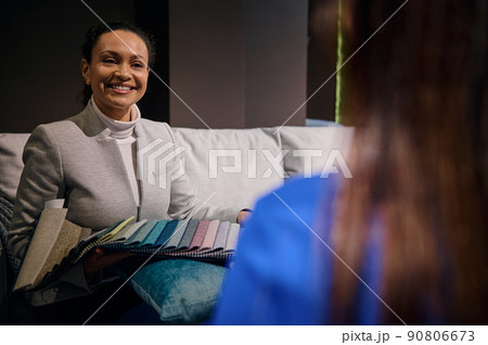 Charming successful sales manager, interior designer working with customers, showing them a palette of colorful fabric samples of various texture and quality for sofa upholstery 90806673