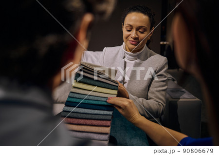 Confident clerk in interior design showroom showing to customers fabric samples for sofa restoration and upholstery. Home improvement and renovation 90806679