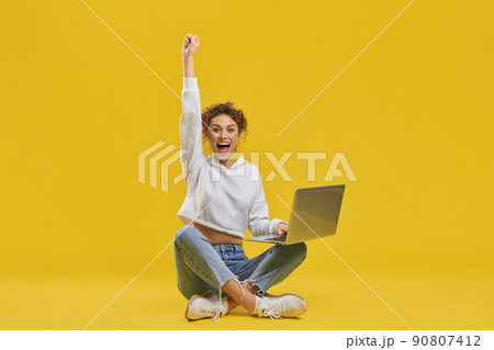 Excited woman celebrating victory, looking at netbook screen inside. Front view of happy female freelancer enjoying successful startup, raising hand, isolated on orange background. Concept of emotion. Excited woman celebrating victory, looking at netbook screen inside. Front view of happy female freelancer enjoying successful startup, raising hand, isolated on orange background. Concept of emotion. 90807412