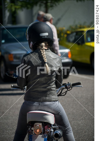 Portrait on back view of blond girl sitting on vintage motorbike in the street 90807424