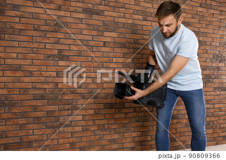 Operator with professional video camera near brick wall, space for text 90809366