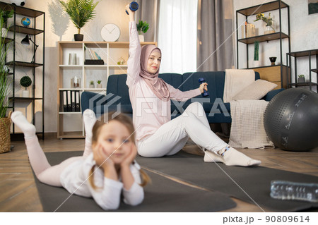 Attractive positive muslim mom doing sports using dumbbells while her cute little girl is resting 90809614