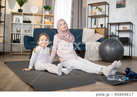 Muslim mother doing sports exercise at home together with funny little daughter Muslim mother doing sports exercise at home together with funny little daughter 90809617