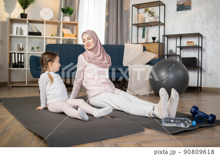 Muslim mother doing sports exercise at home together with funny little daughter Muslim mother doing sports exercise at home together with funny little daughter 90809618