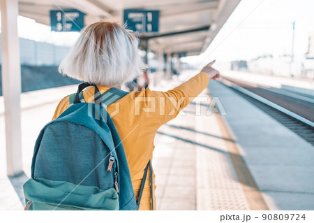 European Travel 50s female with trip backpack shows direction to tourist away at train platform station 90809724