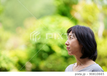 緑の中でTシャツを着て寂しそうに微笑む中年女性　 90810665