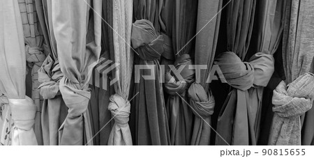 Curtain and fabric for drapery and interior decoration. Samples of fabrics in the store are hung vertically and tied in knots. Curtains in the showcase. Curtain monochrome black, gray and white color. Curtain and fabric for drapery and interior decoration. Samples of fabrics in the store are hung vertically and tied in knots. Curtains in the showcase. Curtain monochrome black, gray and white color. 90815655