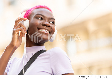Low angle view portrait with copy space of a smiling afro woman using headphones on the street 90818546
