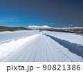 青空のもと雪山へ続く一直線の雪の白い道 90821386