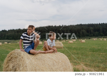 little caucasian adorable boys sitting on haysack in a field on summer time with straw in mouth. Karelia region, Russia 90821961