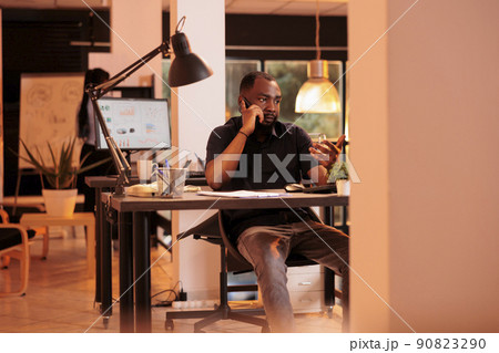 Young employee using mobile phone to call manager at job, talking on phone line to do research project with data report and documents. Having remote discussion with smartphone during sunset. Young employee using mobile phone to call manager at job, talking on phone line to do research project with data report and documents. Having remote discussion with smartphone during sunset. 90823290