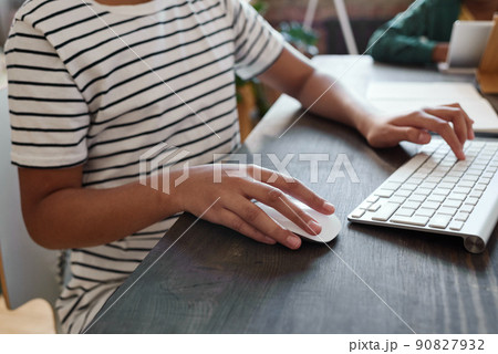 Close-up of African girl using computer mouse and keyboard while sitting at table during her online study 90827932