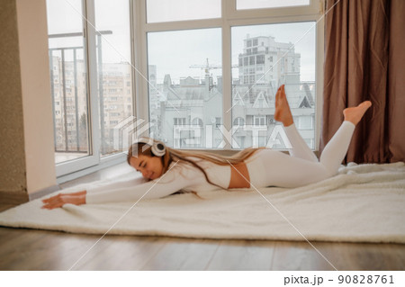Side view portrait of relaxed woman listening to music with headphones lying on carpet at home. She is dressed in a white tracksuit. Side view portrait of relaxed woman listening to music with headphones lying on carpet at home. She is dressed in a white tracksuit. 90828761