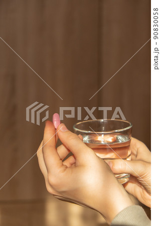 Female hand holding glass of water and pink pill. Collagen supplement for nutrition. Healthy eating lifestyle. Taking vitamins or nutritional supplements. Preventive medicine. Healthcare and wellbeing 90830058