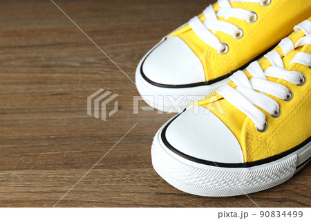 Pair of yellow sneakers on wooden background 90834499