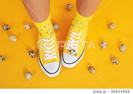 Female legs in socks with eggs and sneakers on yellow background with quail eggs 90834888