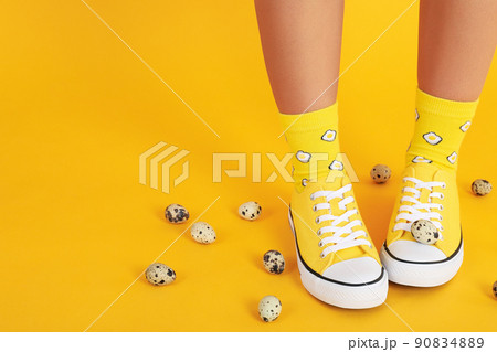 Female legs in socks with eggs and sneakers on yellow background with quail eggs 90834889