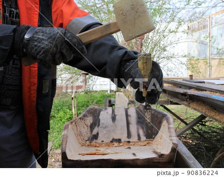 carpenter working with a mallet and a chisel outdoors in a rural yard making a gold pan from solid wood, creating a digging pan in a home workshop setting using hand tools 90836224