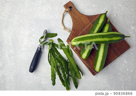 Peeled cucumbers on a wooden cutting board with a vegetable peeler and peels 90836866