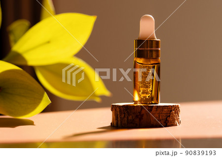Cosmetic amber glass dropper bottle on wooden podium with oil, serum or fruit peeling in the sunlight. Green ruscus, soft focus. Beauty product presentation, natural background. Front. Mockup concept  90839193