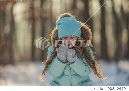 girl blows on the snow which is on her mittens 90840449