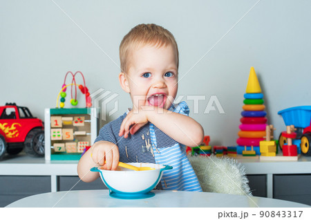 Toddler boy eats with spoon and is covered in food. Baby food, food allergies, self-feeding.... 90843317