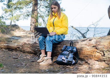 Distance learning online education and work. Woman girl working office work remotely from forest sitting on a log in front of the lake. Using laptop or computer Distance learning online education and work. Woman girl working office work remotely from forest sitting on a log in front of the lake. Using laptop or computer 90844353