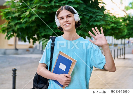 Smiling teenage male student with textbooks looking at camera outdoor 90844690