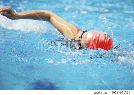 The athlete swims in the pool in a red swimming cap. A man swims in blue water. 90844732