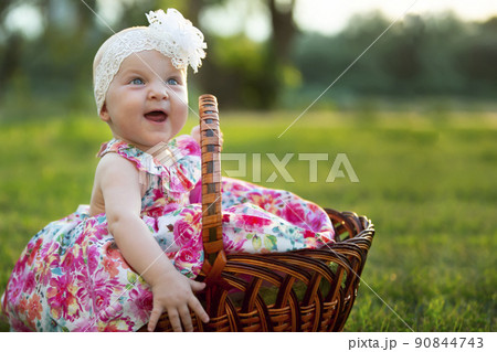 Happy little girl sits in a basket and laughs. A beautiful child. Little baby up to a year old on a summer meadow. Happy little girl sits in a basket and laughs. A beautiful child. Little baby up to a year old on a summer meadow. 90844743