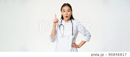 Healthcare and medical concept. Asian woman doctor raising finger, found solution, treatment for patient, pointing up and looking enthusiastic, white background 90846817