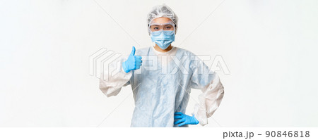 Asian female doctor or nurse wearing personal protective equipment and rubber gloves, medical face mask, showing thumbs up, vaccination and covid-19 campaign concept 90846818