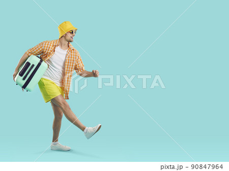 Happy excited guy tourist or vacationer, goes carrying travel suitcase on light blue background. 90847964