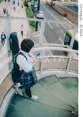 ギターとスマートフォン持った制服姿の女子高生と街 90848103