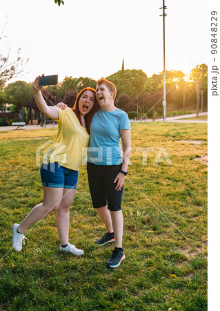 two smiling friends taking a selfie, in a public park in the city at sunset. young girl couple enjoying the summer outdoors.concept of friendship and companionship. vertical 90848229