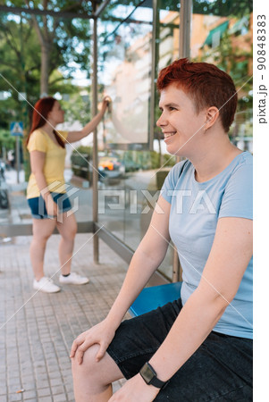 young girl sitting, waiting at the bus station in the big city. woman outdoors at the bus stop while waiting for the tram. vertical. young girl sitting, waiting at the bus station in the big city. woman outdoors at the bus stop while waiting for the tram. vertical. 90848383