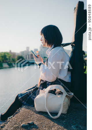 ギターとスマートフォン持った制服姿の女子高生と街 90848689