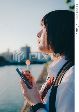 ギターとスマートフォン持った制服姿の女子高生と街 90848814