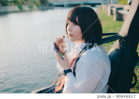 ギターとスマートフォン持った制服姿の女子高生と街 90848817