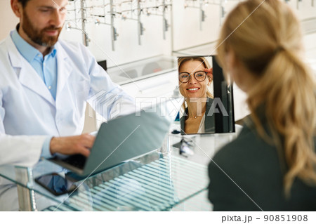 Woman looks in the mirror trying to choose glasses on the advice of an ophthalmologist 90851908