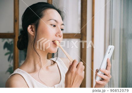 スマホを見ながら歯磨きをする女性・竹歯ブラシを使う女性 スマホを見ながら歯磨きをする女性・竹歯ブラシを使う女性 90852079