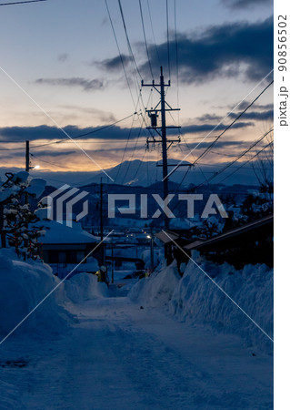 夕暮れ時家に帰る途中、住宅街の雪に覆われた道路を下っていく 90856502