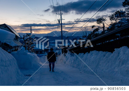 夕暮れ時住宅街の雪に覆われた道路を降りていく人 90856503