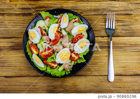 Tasty tuna salad with eggs, lettuce and fresh vegetables on wooden table. Top view Tasty tuna salad with eggs, lettuce and fresh vegetables on wooden table. Top view 90860296