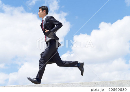 青空のもとでカバンを持って走るスーツ姿のビジネスパーソン 90860880