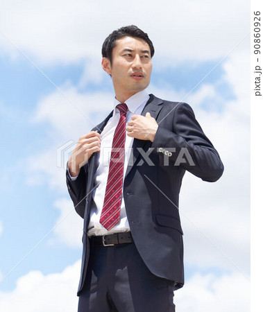青空のもと真剣な表情で上着の襟を直すビジネスパーソン 90860926