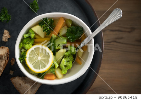 Vegetarian vegetable soup with carrots, broccoli and parsley in a light bowl on a metal tray on a wooden table Vegetarian vegetable soup with carrots, broccoli and parsley in a light bowl on a metal tray on a wooden table 90865418