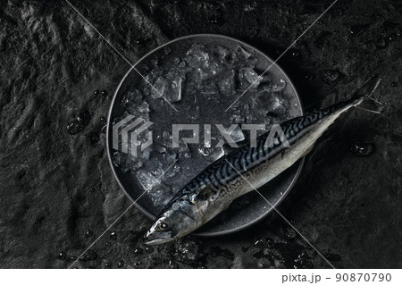 Top view of fresh raw mackerel in ice rocks on textured black background 90870790