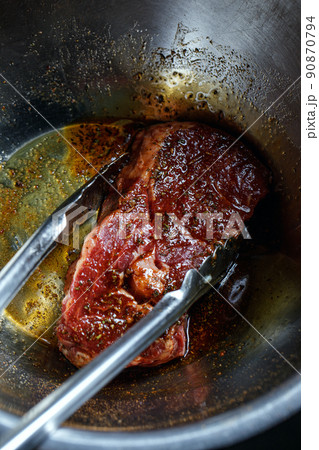 Silver serving kitchen tongs holding raw meat beef steak marinated and prepared for grilling on rack charcoal stove 90870794