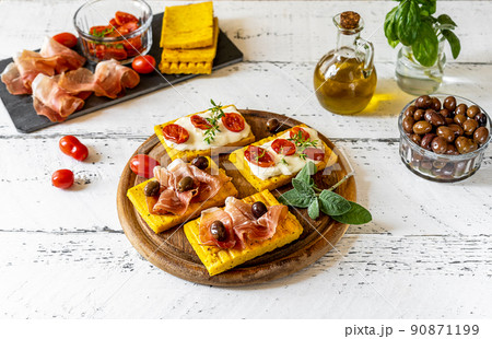 Grilled polenta with stracchino cheese, tomatoes, herbs, speck and olive. White wooden background, ingredients  90871199